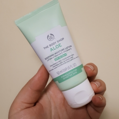 Rosie's hand holding a green and white tube of The Body Shop's Aloe Lotion