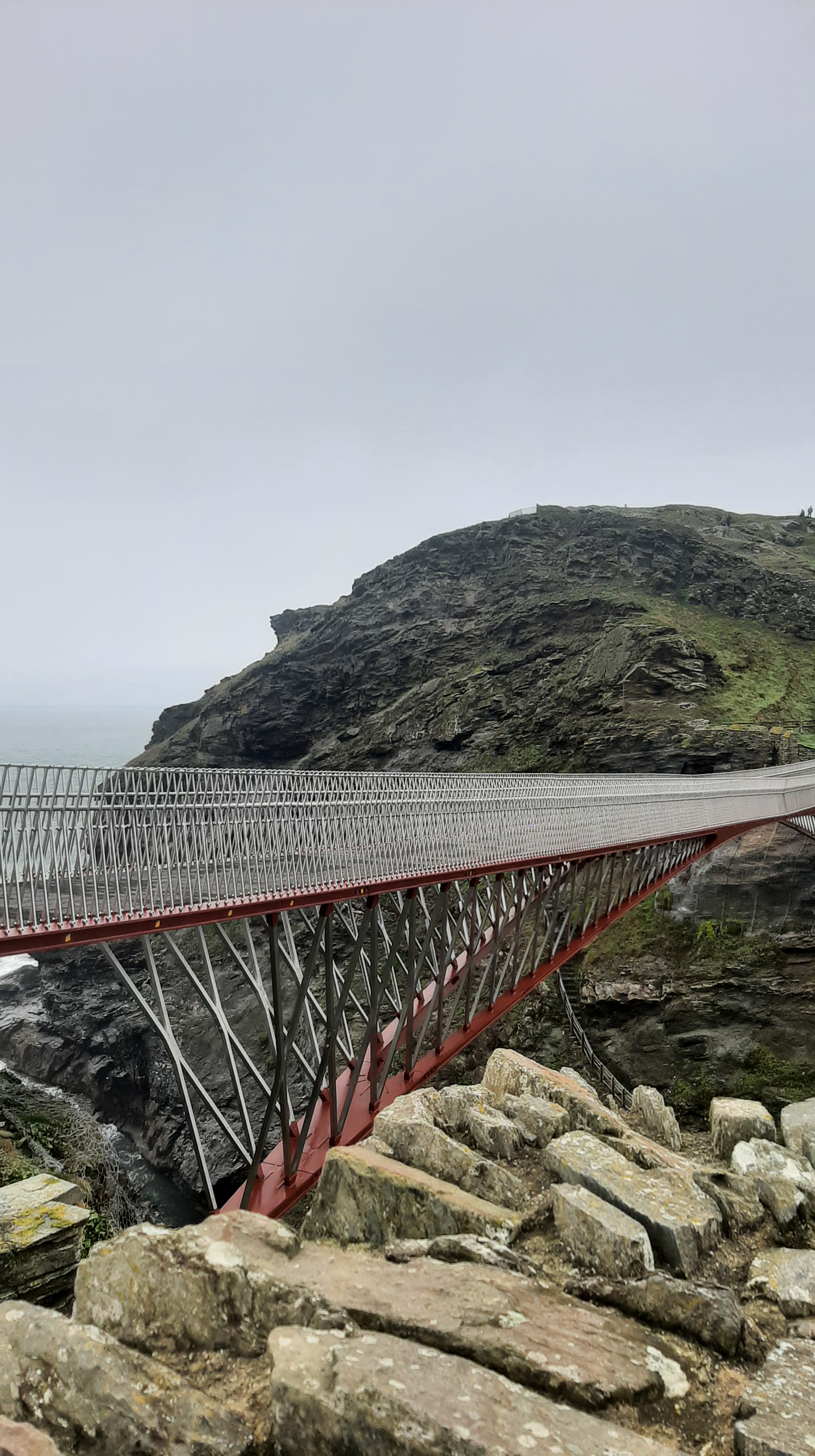 The red and grey bridge that joins the mainland with the island of Tintagel Castle.