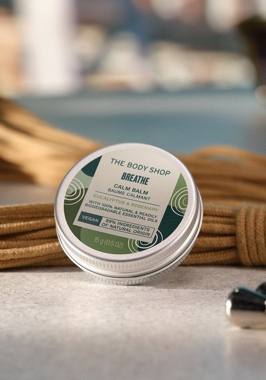 A tin of The Body Shop's Breathe Calm Balm. It is silver in colour with a green and cream sticker. There is brown rope in the background.