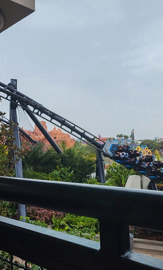 An image of a rollercoaster ride vehicle speeding into the image along a turning track. They sky is grey behind it and the track is black. There are people on the vehicle.